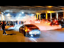 a group of cars are doing a burnout under a bridge .