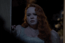 a woman with red hair and a white dress is standing in a dark room