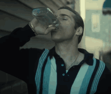 a man in a striped shirt is drinking from a glass