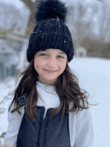 a little girl wearing a black hat with pearls on it stands in the snow