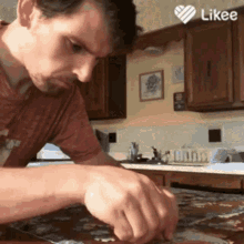 a man in a red shirt is sitting at a table in a kitchen with a likee heart above him