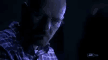 a man in a plaid shirt is sitting in a dark room .