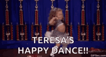 a little girl is dancing on a stage with trophies in the background and the words `` teresa 's happy dance '' .