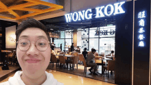 a man stands in front of a restaurant called wong-kok