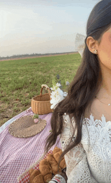 a woman in a white lace top is sitting on a picnic blanket in a field