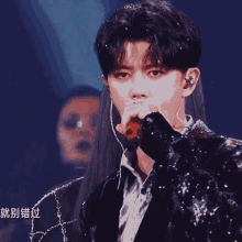 a man in a sequined jacket sings into a microphone with chinese writing behind him