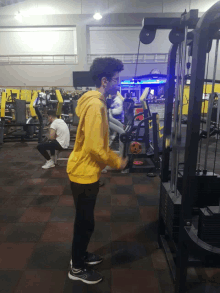 a young man wearing a yellow hoodie is using a machine in a gym