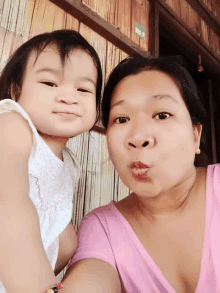 a woman in a pink shirt is holding a little girl and blowing a kiss