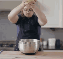 a man in a blue shirt is holding a bowl over a metal bowl that has the letter t on it