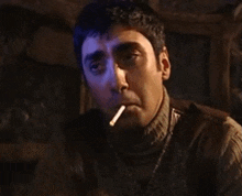 a man is smoking a cigarette in a dark room while looking at the camera .