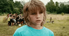 a young boy in a blue shirt is standing in a field with a group of children playing soccer in the background .