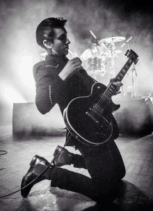 a black and white photo of a man playing a guitar on a stage