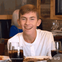 a young man is smiling while sitting at a table with a plate of food and a glass of soda