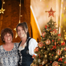 two women pose in front of a christmas tree with a star on top