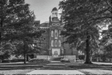 a black and white photo of a large brick building surrounded by trees and grass .