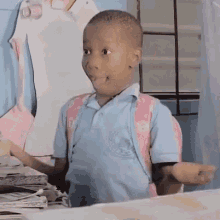 a young boy in a blue shirt and pink backpack is making a funny face while sitting at a table .