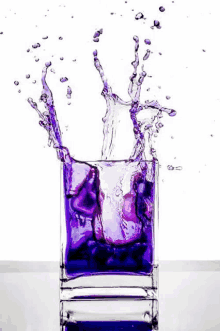 a purple liquid is splashing out of a glass of water .