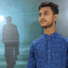 a young man in a blue shirt stands in front of a reflection of a man riding a bike