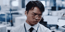 a man wearing glasses and a lanyard is sweating in an office