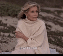 a woman in a white sweater is sitting on a blanket with the words wind blowing behind her