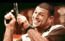 a man is smiling and holding a gun in his hand .