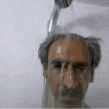 a man with a mustache is taking a shower with water coming out of a shower head .