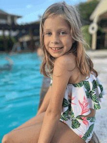 a little girl in a bikini is sitting on the edge of a swimming pool