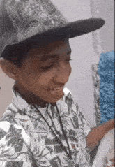 a young boy wearing a hat and a floral shirt looks at something