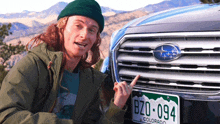 a man pointing at a subaru with a license plate that says bzo-094