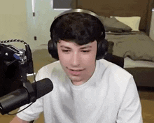 a young man wearing headphones and a white shirt is sitting in front of a microphone in a bedroom .