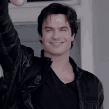 ian somerhalder is wearing a black leather jacket and a black shirt and smiling with his arm in the air .