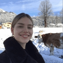 a woman is smiling in front of a cow in a snowy field .