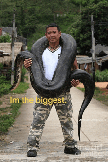 a man holding a large black snake with the words im the biggest on the bottom