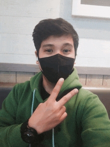 a man wearing a green hoodie and a black face mask is giving the peace sign