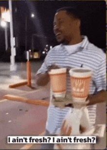 a man in a striped shirt is holding a tray with two cups of coffee and a bag of food .