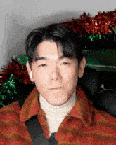 a man wearing a red sweater and a white turtleneck is sitting in a car with christmas decorations in the background