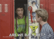 two men are standing next to each other in front of a red locker and talking to each other .