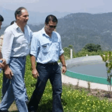 a group of men are walking through a grassy field with mountains in the background