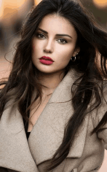 a woman with long hair and red lipstick is wearing a tan coat