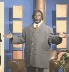 a man in a suit and tie is standing in front of a chair with his arms outstretched