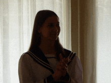 a girl in a sailor uniform applauds in front of a window