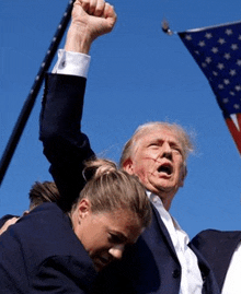 a man in a suit is holding a woman 's fist in the air in front of a flag .