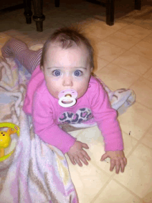 a baby with a pacifier in her mouth wears a pink sweater with a leopard print on it