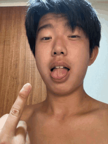 a shirtless young man sticks his tongue out and shows his middle finger