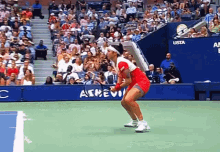 a woman in a red dress is holding a tennis racquet on a tennis court in front of a sign that says us open