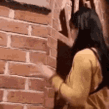 a woman in a yellow dress is standing in front of a brick wall and talking on a cell phone .