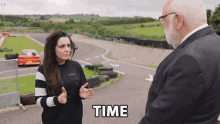 a man in a suit talks to a woman in a black and white sweater with the word time above them