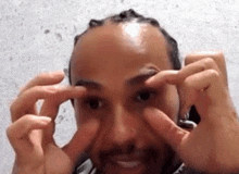 a man with dreadlocks is covering his eyes with his hands and smiling .