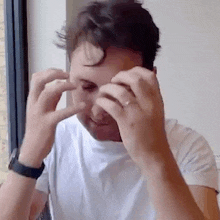 a man wearing a white shirt and a watch is covering his face with his hands