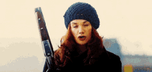 a woman wearing a hat is holding a gun .